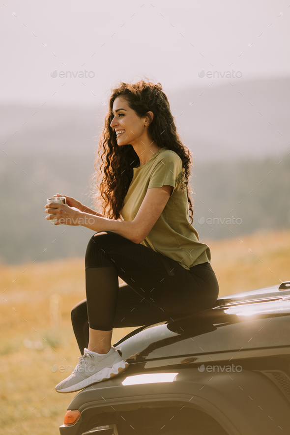 Young woman relaxing on a terrain vehicle hood at countryside - Stock Photo - Images