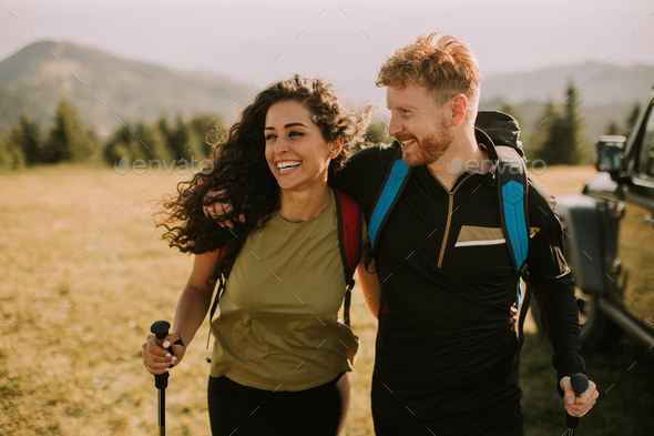 Smiling couple walking with backpacks over green hills - Stock Photo - Images