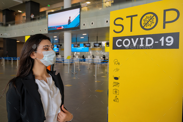 Girl at the airport waits for a flight in front of stop COVID banner