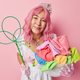 Horizontal shot of pleased Asian woman with pink hair does housework poses with laundry and carpet - PhotoDune Item for Sale