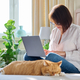 Mature woman using laptop sitting on couch at home, with relaxed sleeping ginger cat - PhotoDune Item for Sale