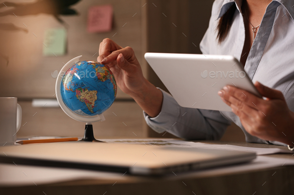 Unrecognizable businesswoman examining globe while surfing the net on touchpad.