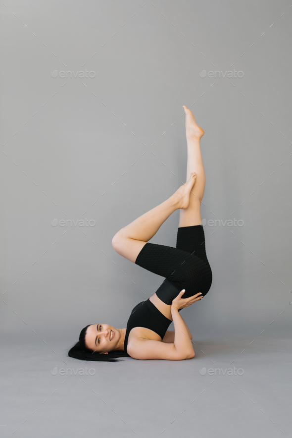 Athletic young woman doing fitness or yoga, lying on the floor and lifting her legs up