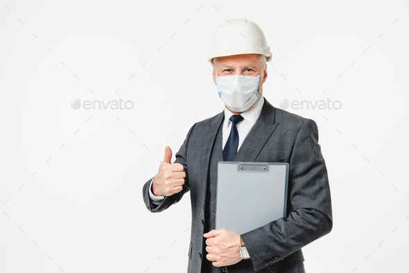 Caucasian inspector in hardhat and protective face mask showing thumb up, coronavirus concept