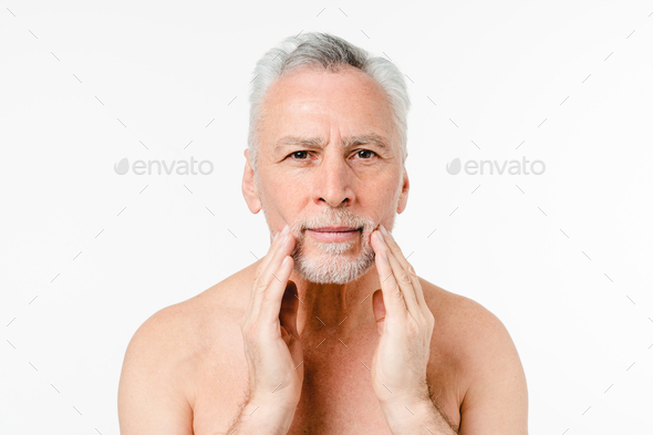 Caucasian shirtless naked elderly man going to shave beard, touching face, applying aftershave balm - Stock Photo - Images