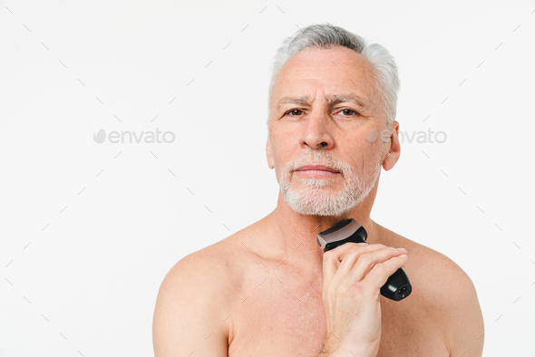 Mature elderly senior naked shirtless man with grey hair shaving beard with electric razor trimmer - Stock Photo - Images