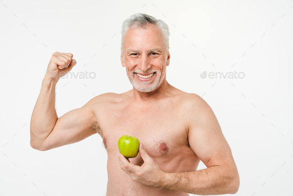 Strong powerful mature elderly senior shirtless naked man holding green apple with toothy smile - Stock Photo - Images