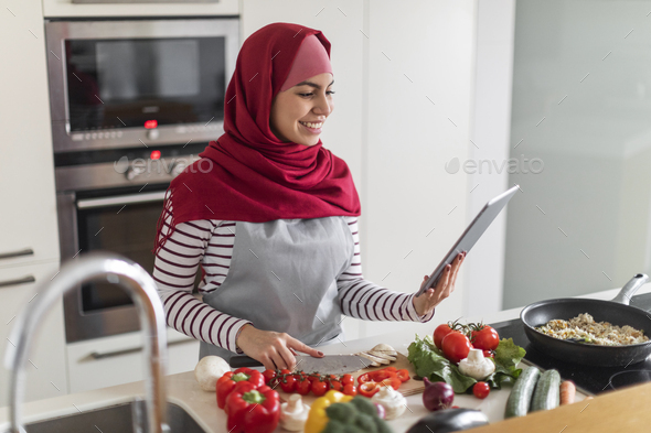 Happy muslim woman enjoying cooking at home, using digital tablet - Stock Photo - Images