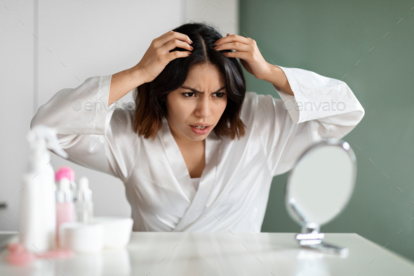 Angry lady in white bathrobe sitting in bedroom, checking hair - Stock Photo - Images