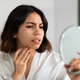 Upset young woman looking at mirror and touching her face - PhotoDune Item for Sale