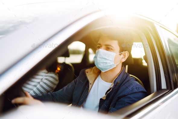 Woman wearing a medical sterile mask in a taxi car on a backseat looking sideway out of open window.