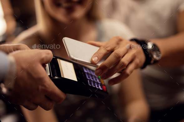 Close up of customer making contactless payment to a waiter in a cafe.