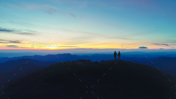 The man and woman standing on the mountain on the sunset background ...