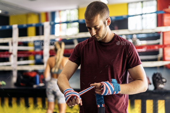 Standing adult man wrapping hands with clored boxing wrap for training in the gym