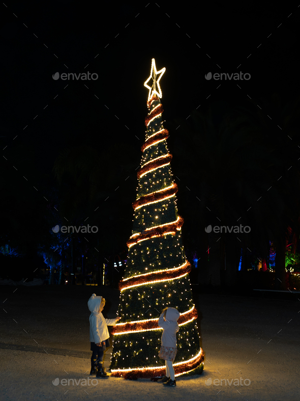 Children touching conical Christmas tree in city - Stock Photo - Images