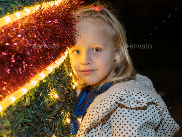 Blond girl leaning on Christmas tree with garlands - Stock Photo - Images