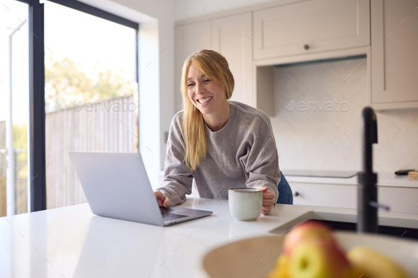 Woman At Home Working On Laptop On Counter In Kitchen
