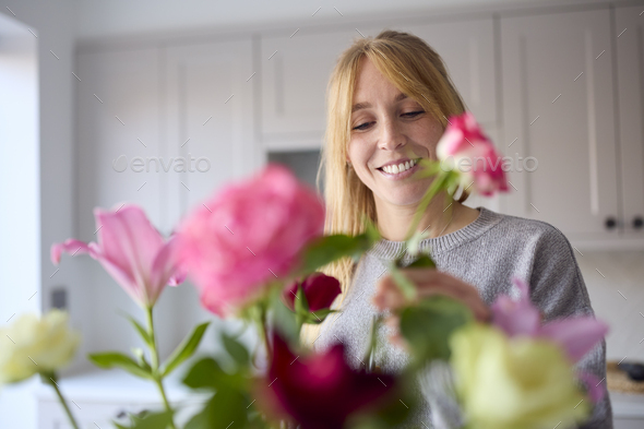 Woman Arranging Bunch Of Flowers On Kitchen Counter In New Home - Stock Photo - Images