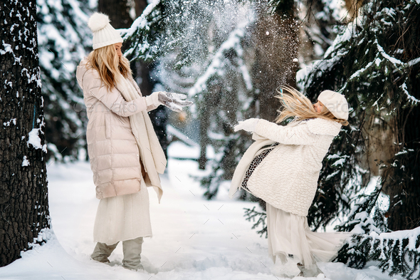Handsome mother and daughter are having fun outdoor in winter time. Playing with snow in forest - Stock Photo - Images