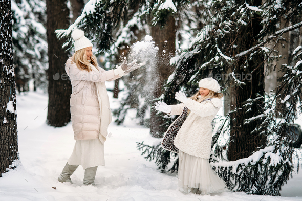 Handsome mother and daughter are having fun outdoor in winter time. Playing with snow in forest  - Stock Photo - Images