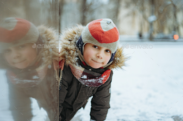 winter portrait of cute caucasian boy of elementary age in knit hat with pompom in city - Stock Photo - Images