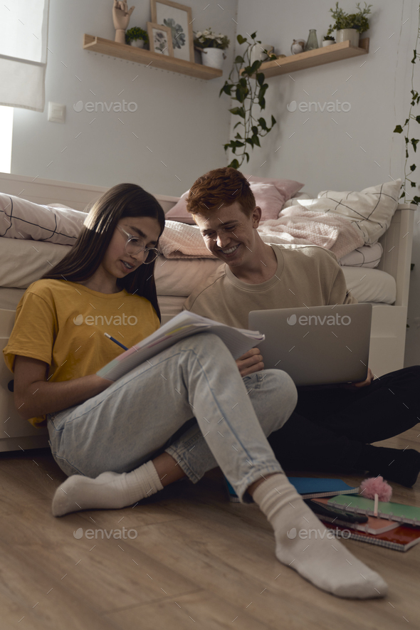 Two caucasian teenagers sitting on floor and learning from books and laptop - Stock Photo - Images