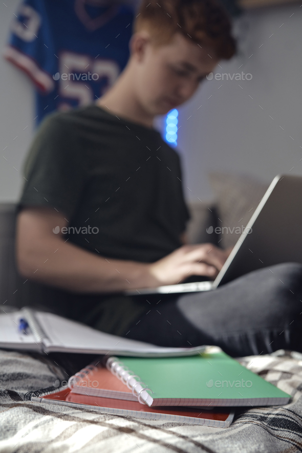 Caucasian teenager boy sitting on bed and learning using laptop - Stock Photo - Images