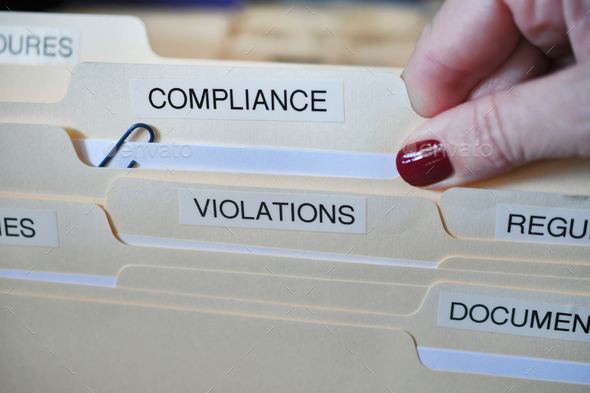 A female hand removing a Compliance folder from a cabinet full of files and folders inoffice at work