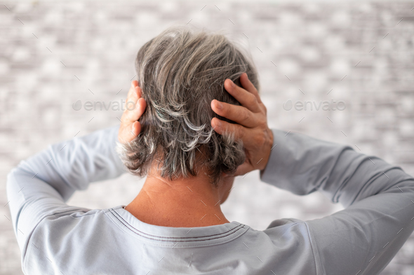 Frustrated senior woman with hands on ears, standing at home alone, senior woman suffering