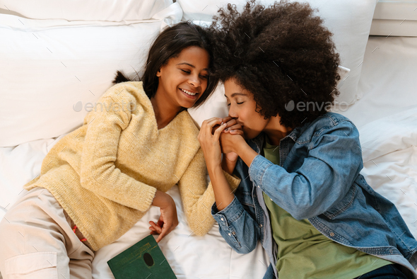 Black woman kissing her daughter\'s hand while lying on bed