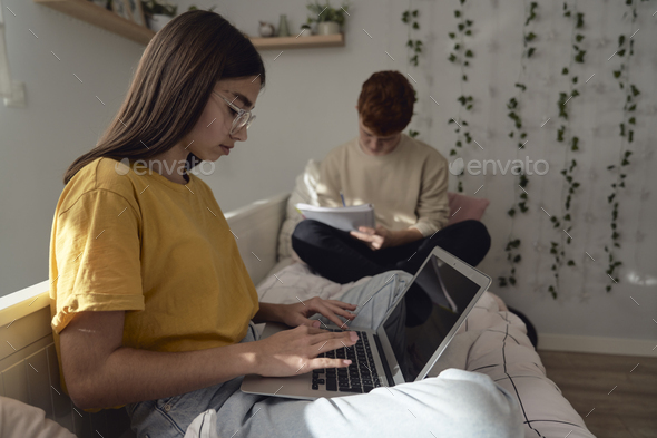 Two caucasian teenagers sitting on floor and learning from books and laptop in silence - Stock Photo - Images
