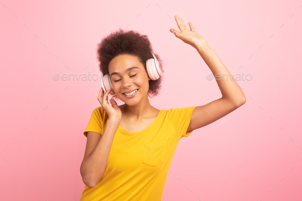 Satisfied relaxed young african american curly woman in casual, wireless headphones, dancing, enjoy - Stock Photo - Images
