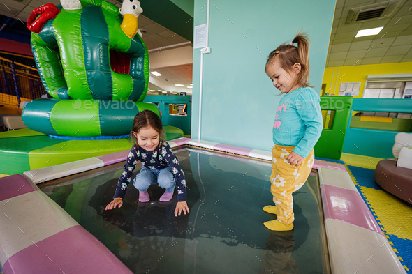 Happy sisters playing at indoor play center playground in water trampoline.