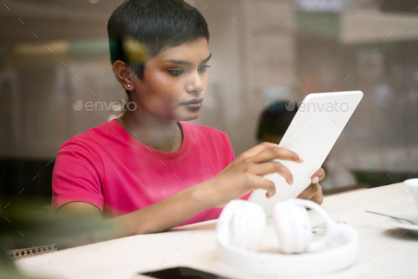 Indian woman using digital tablet watching training courses, communication online sitting in cafe