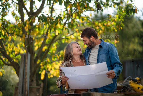 Happy mature couple with architectural blueprints of their future house, standing outdoors. - Stock Photo - Images