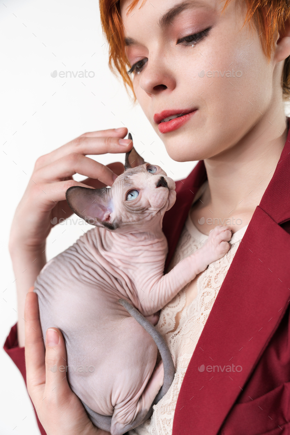 Hipster young redhead woman with short hair gently hugging to her chest Canadian Sphynx Cat - Stock Photo - Images