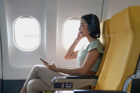 Young female listening favourite songs during flight in first class cabin using mobile playlist and - Stock Photo - Images