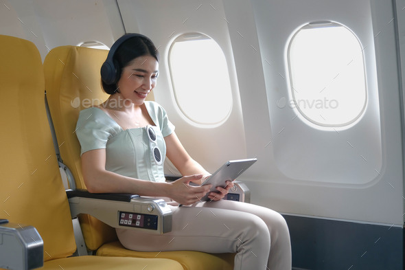 Young female listening favourite songs during flight in first class cabin using mobile playlist and - Stock Photo - Images