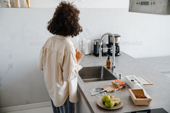 African american young woman listening to music while making breakfast