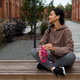 Attractive sportswoman in earphones holding fitness bottle while sittings on bench in city - PhotoDune Item for Sale