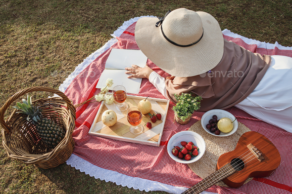Woman laying and reading book on aesthetic picnic outdoors