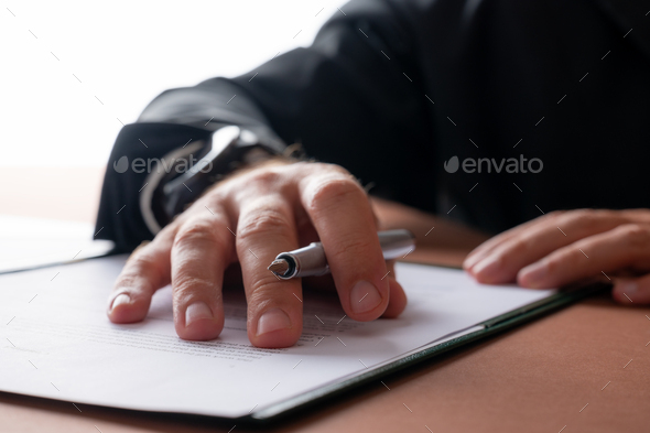 Businessman holding a pen proofreading a contract or document in a folder - Stock Photo - Images