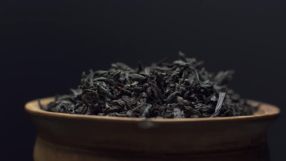 Close up view dry black ceylon tea leaves rotate in a clay bowl on black background alt