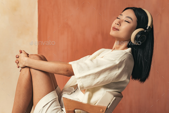 Side view of relaxed asian woman with wireless headphones, listening to meditation music