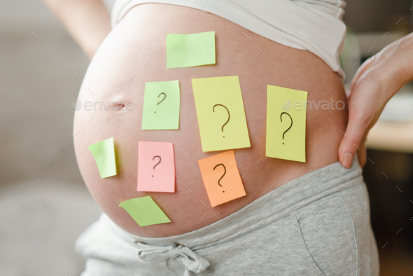Concept of choosing baby name. cropped shot of pregnant woman with question marks on paper stickers - Stock Photo - Images