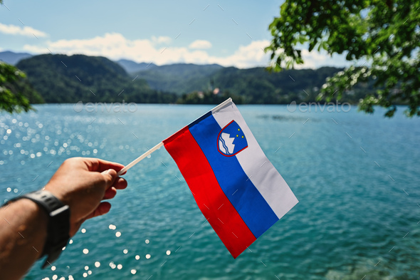 Man hand hold slovenian flag against view of beautiful Bled Lake, Slovenia.