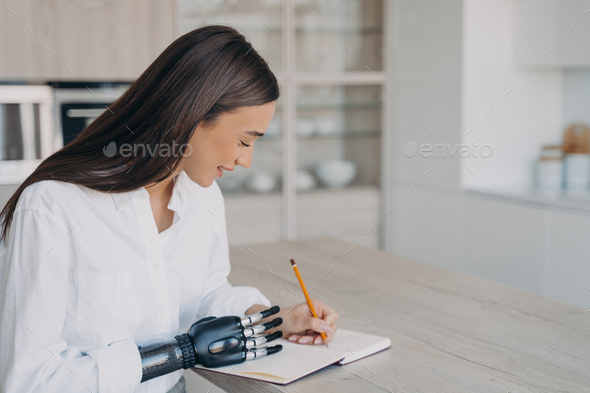 School girl with bionic prosthesis is studying or working remotely and taking notes at the desk.
