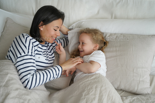 Happy young mom lying in bed with adopted daughter after sleeping ...