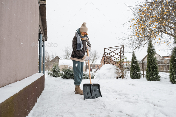 Close-up of a woman cleaning and clearing snow in front of the house on a sunny and frosty day. Clea - Stock Photo - Images