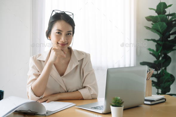 Portrait of businesswoman with laptop while checklist on a document at her office. - Stock Photo - Images